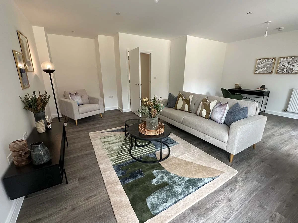 Modern living room with neutral sofa, armchair, abstract green rug, and minimalist decor in a contemporary apartment