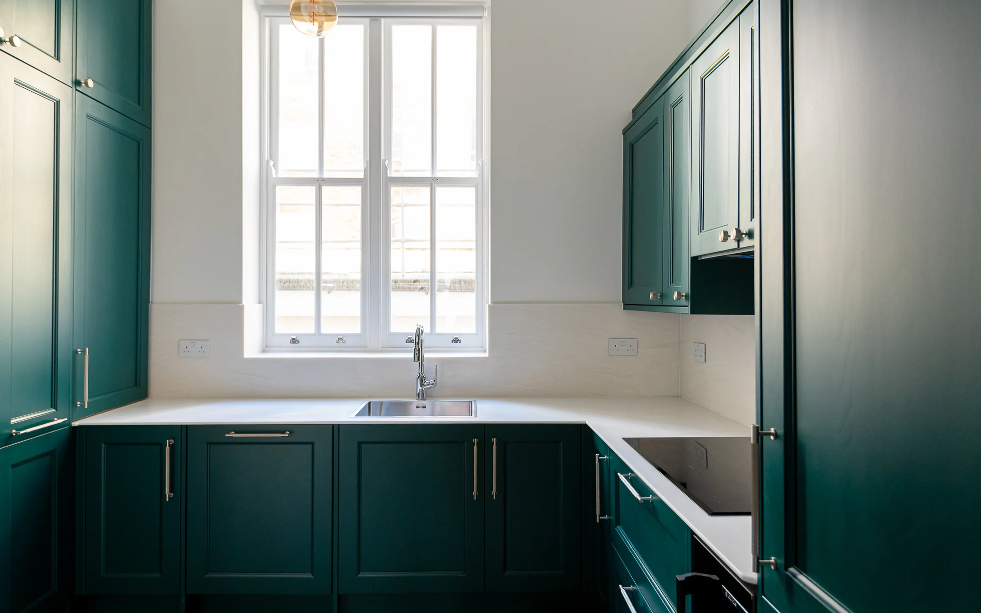 A bespoke luxury kitchen styled by InStyle Direct featuring deep emerald green cabinetry with elegant gold hardware, a white marble countertop, and a classic sash window in Bayswater.