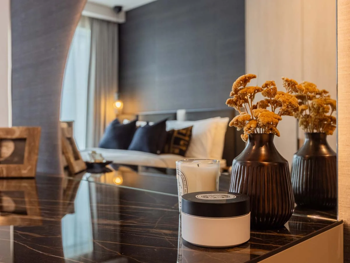 Bedroom dresser with decorative vases, candle, and mirror reflection of bed