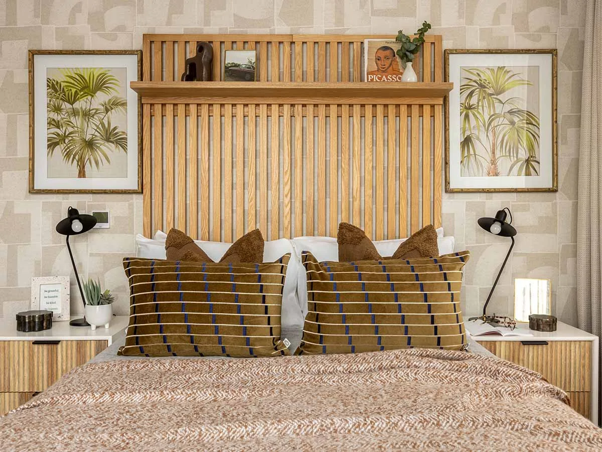 A stylish bedroom at Fulton & Fifth featuring a large slatted oak headboard with a display shelf, geometric wallpaper, and framed palm tree art