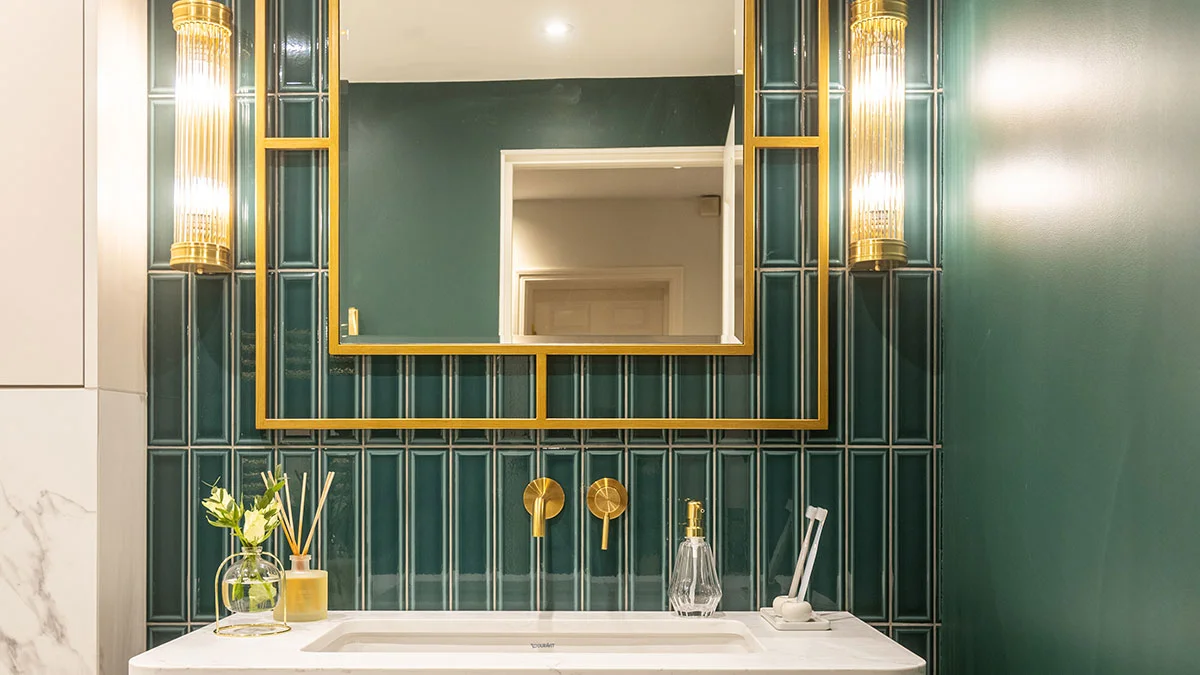 A bespoke luxury bathroom designed by InStyle Direct featuring deep emerald green vertical tiling, a large gold-framed mirror, and premium brass faucets and lighting fixtures in Hyde Park.