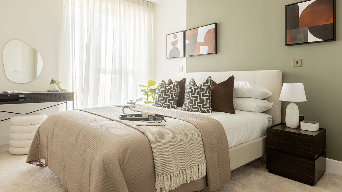 A bespoke bedroom interior by InStyle Direct featuring an olive green feature wall, a cream upholstered headboard, tiered abstract wall art, and floor-to-ceiling sheer white curtains in London