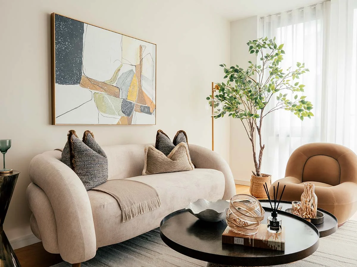 A beautifully designed living room for a homeowner, featuring a plush, curved cream sofa, modern abstract art, and a large indoor tree for a personal touch