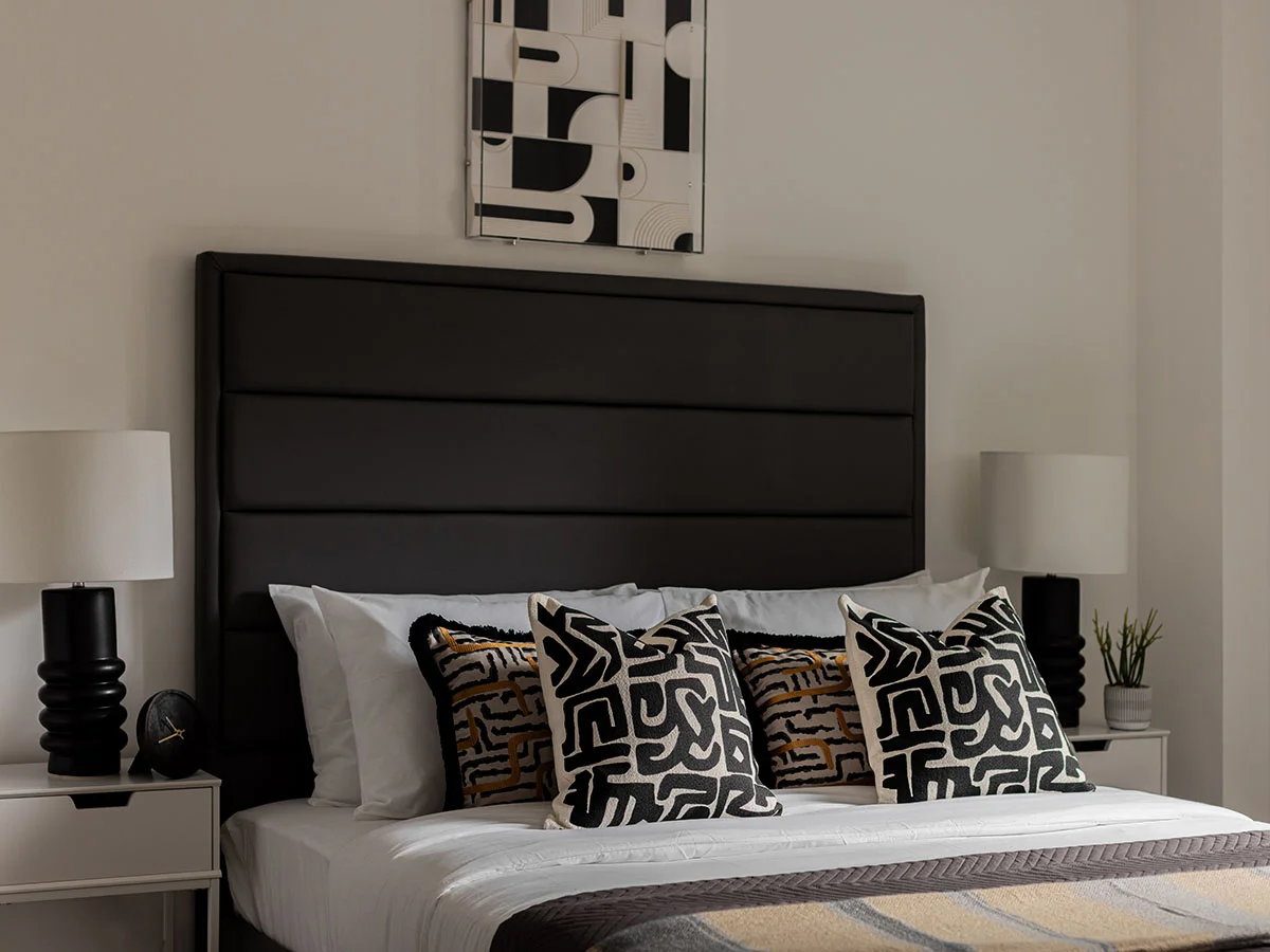 A boutique bedroom interior styled by InStyle Direct featuring a tall black ribbed headboard, monochrome geometric patterned cushions, and symmetrical black textured bedside lamps in Westminster.