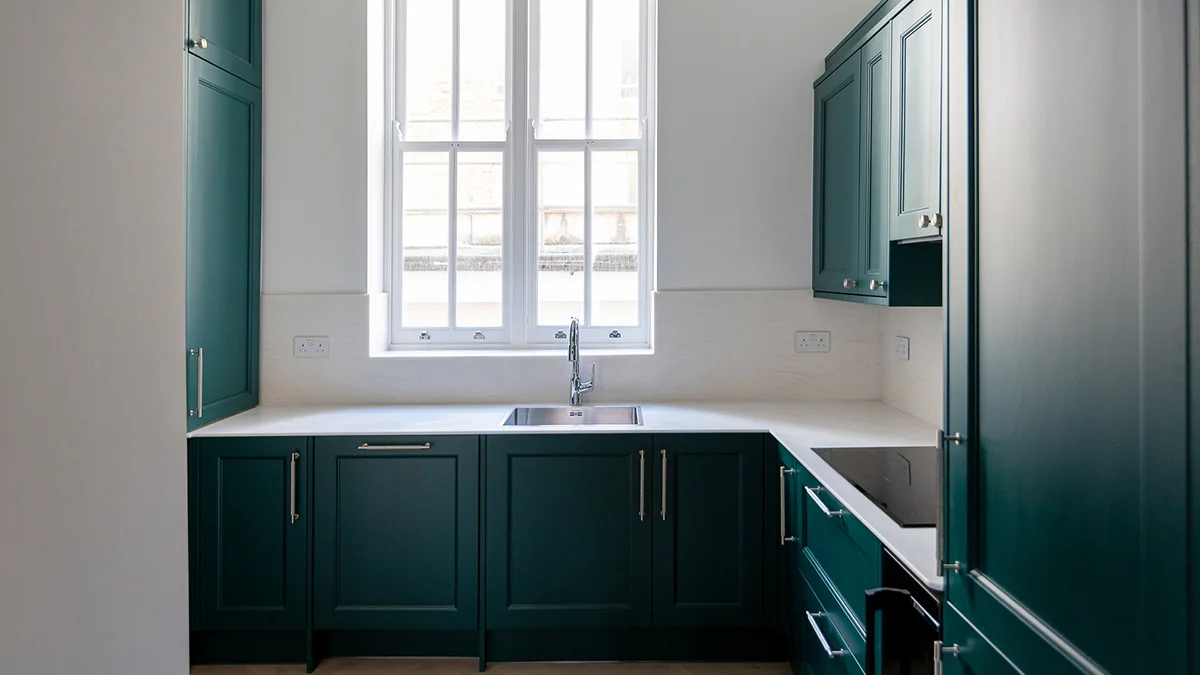 A contemporary kitchen styled by InStyle Direct featuring sleek forest green cabinetry, white marble countertops, a minimalist silver faucet, and a large classic sash window in Bayswater.