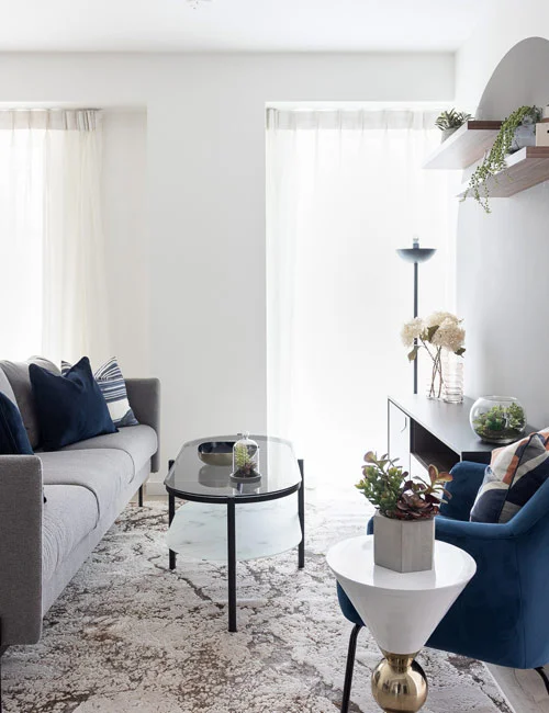 A contemporary living room professionally staged by InStyle Direct featuring a light grey sofa adorned with navy and terracotta velvet cushions, set against a bright minimalist background in Silvertown