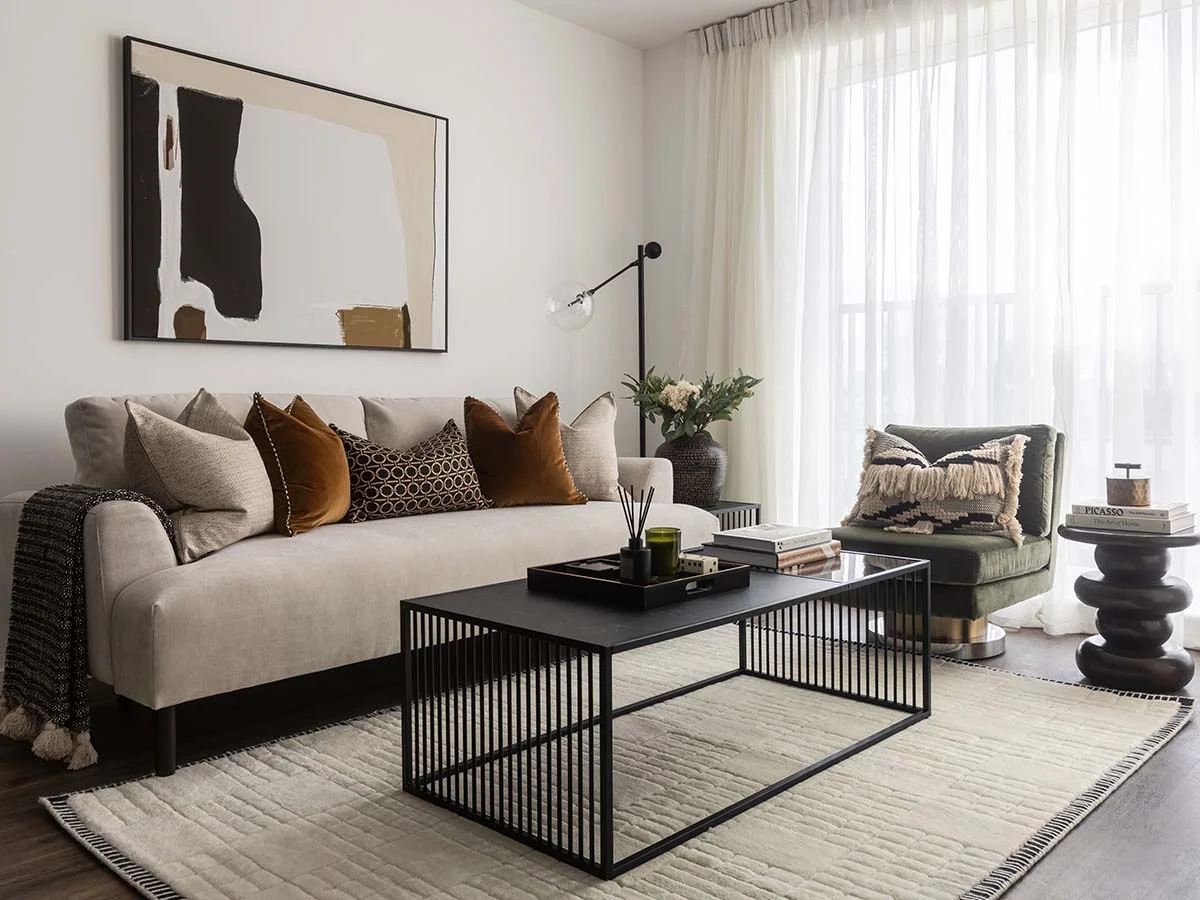 A contemporary living room styled by InStyle Direct featuring a neutral sofa with velvet cushions, a black slatted coffee table, and an abstract oversized wall art piece in London