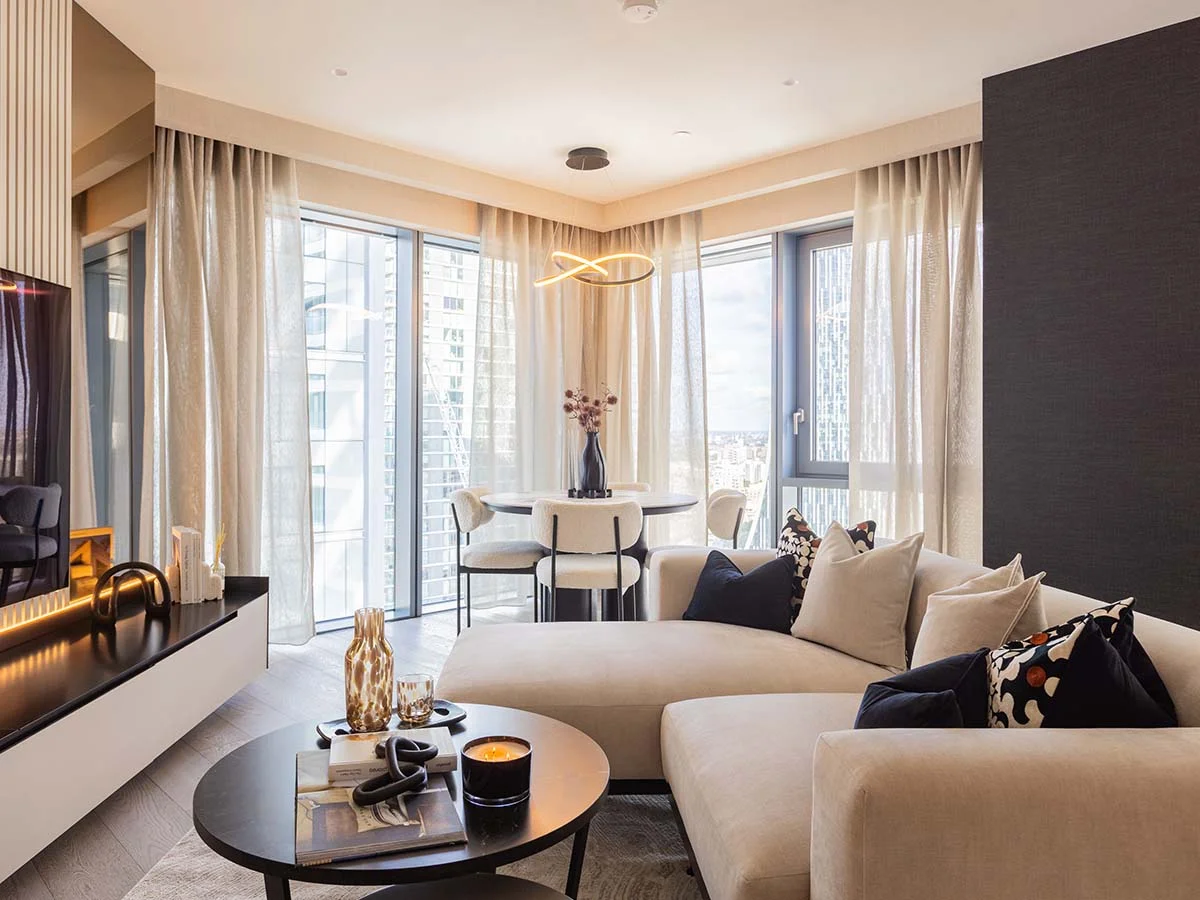 An elevated living room styled by InStyle Direct featuring a white grand piano, a curved cream sofa, and a dining area framed by a window with a direct view of the London Eye