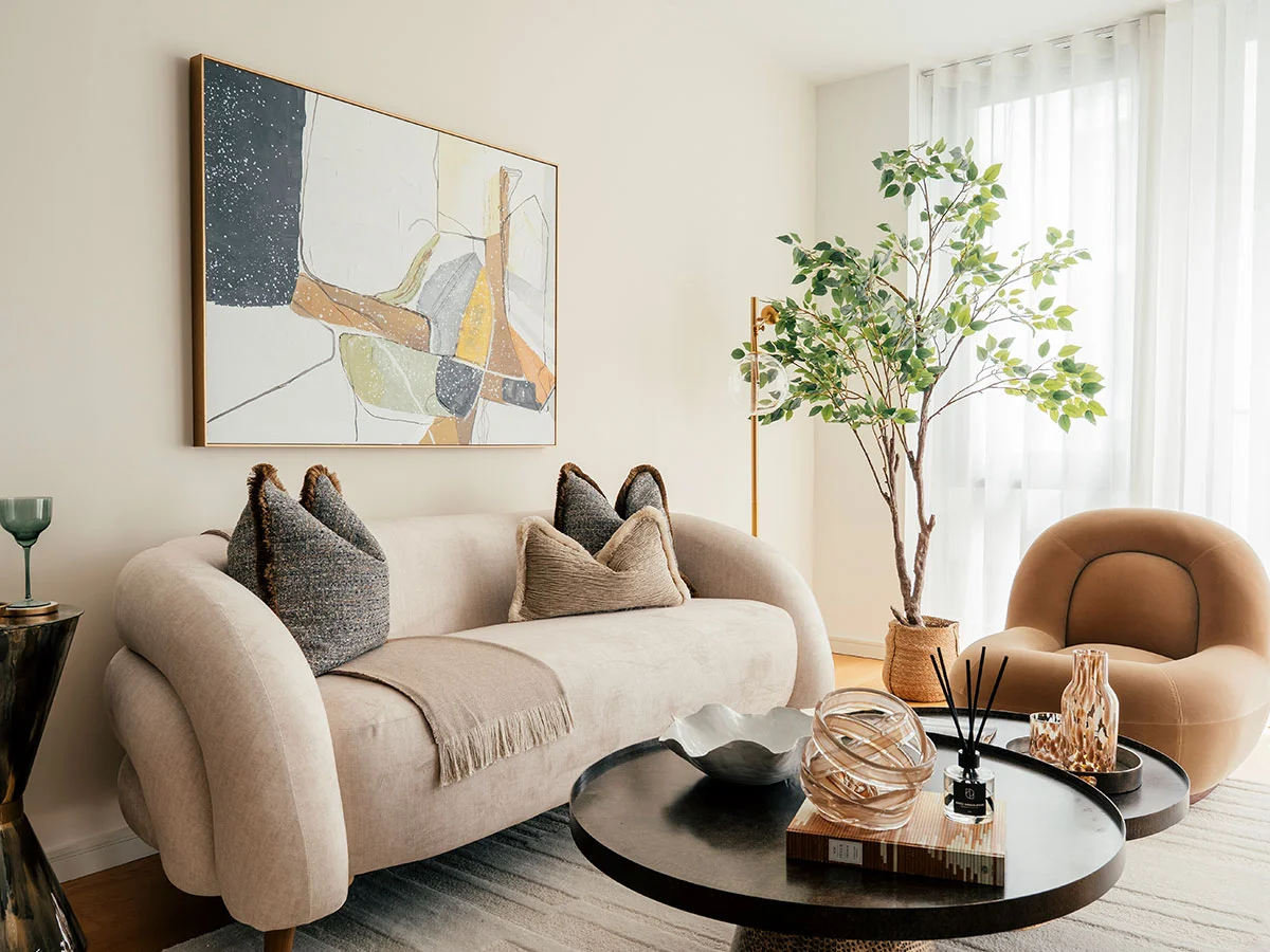 A contemporary living room at the Riverside development, featuring a curved cream sofa, a brown velvet armchair, and abstract wall art
