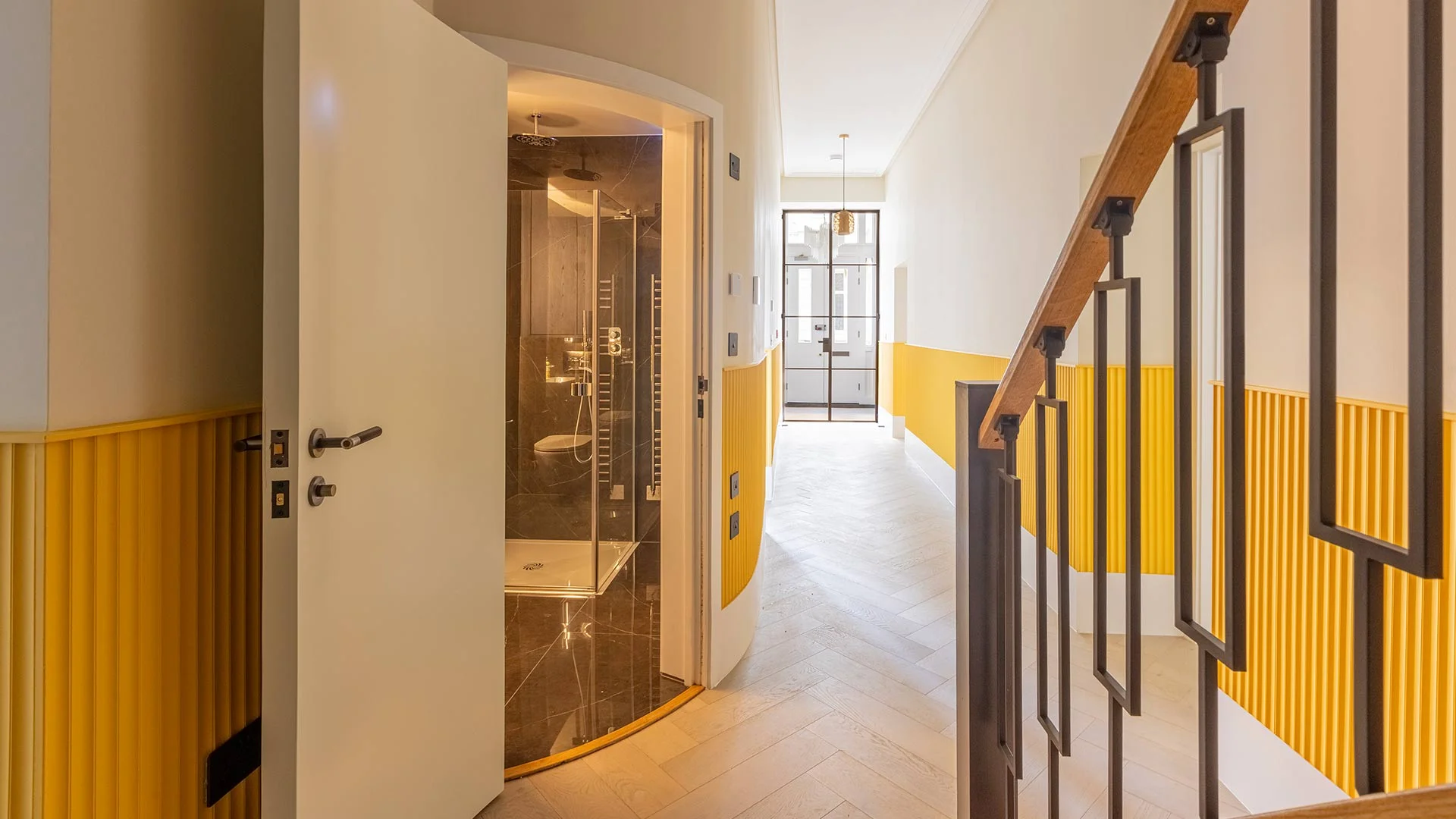 A designer hallway interior styled by InStyle Direct featuring vibrant yellow fluted wall panelling, light herringbone wood flooring, and a view into a sleek black marble bathroom in Bayswater.