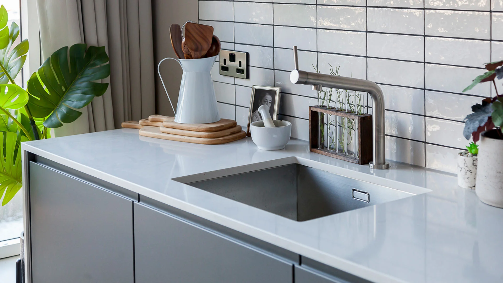 Designer kitchen accessories professionally styled by InStyle Direct featuring a white ceramic pitcher with wooden spoons, stacked cutting boards, and a mortar and pestle against a white tiled backsplash in Stratford.