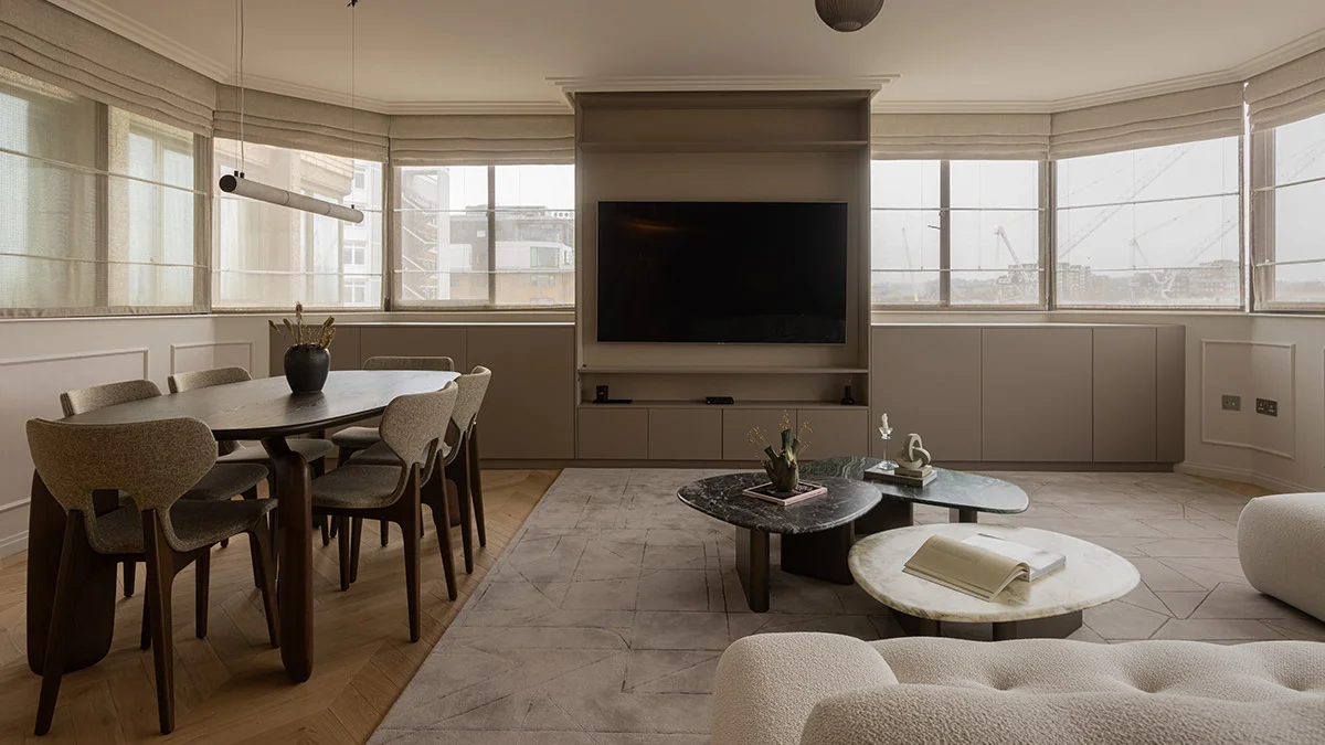 A contemporary open-plan living and dining area in London featuring a bespoke floor-to-ceiling media unit, an oval dark wood dining table with designer chairs, and layered marble coffee tables on a geometric rug.