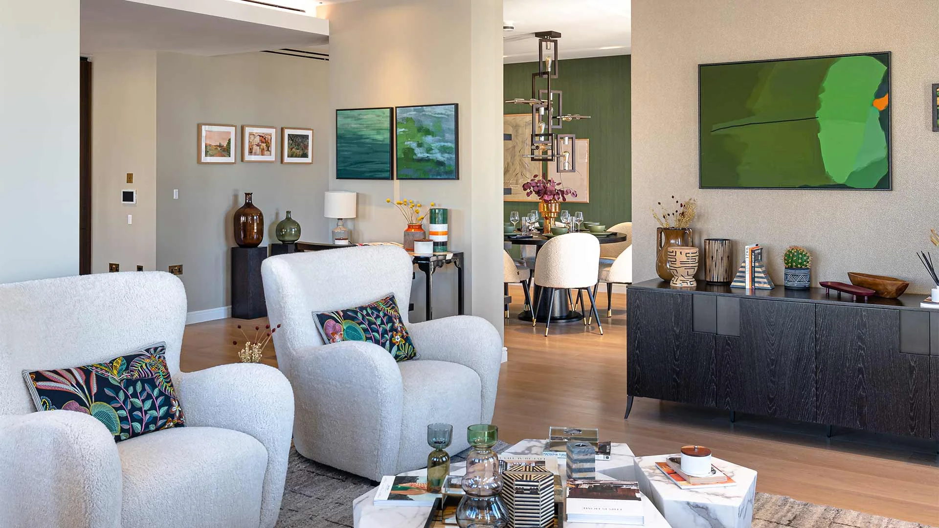 A high-end open-plan living room styled by InStyle Direct featuring white boucle armchairs with botanical cushions, a dark wood sideboard with curated pottery, and a marble coffee table in Lincoln Square.