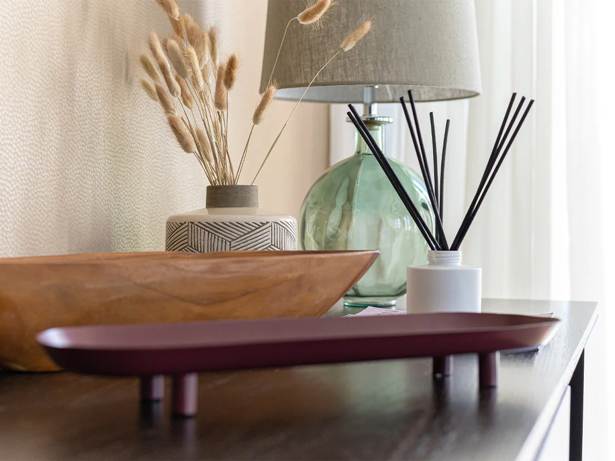 Designer sideboard styling by InStyle Direct featuring a textured geometric vase with dried bunny tail grass, a green glass table lamp, and a white reed diffuser on a dark wood console.