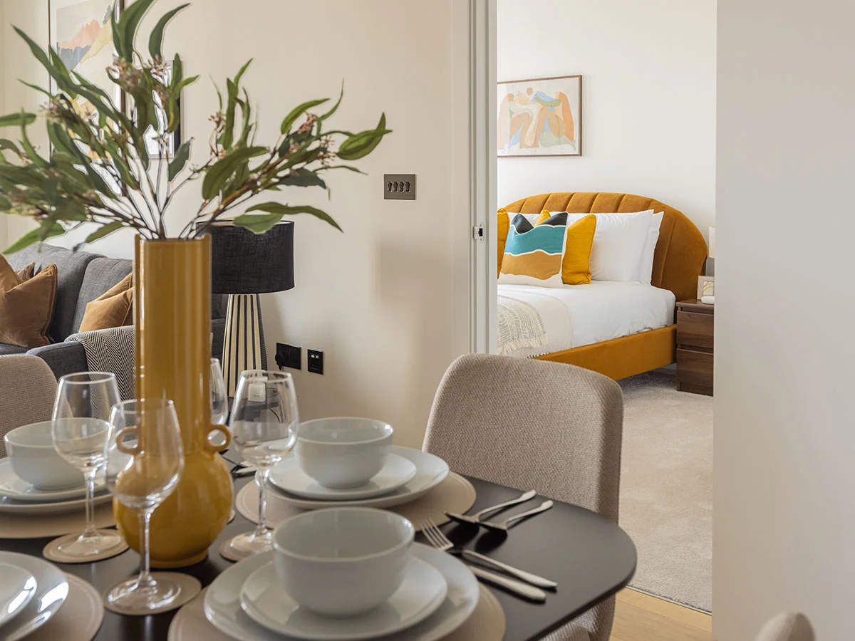 A view from the dining table into a bedroom at White City, highlighting the yellow vase centerpiece and the bright orange curved headboard inside the room 