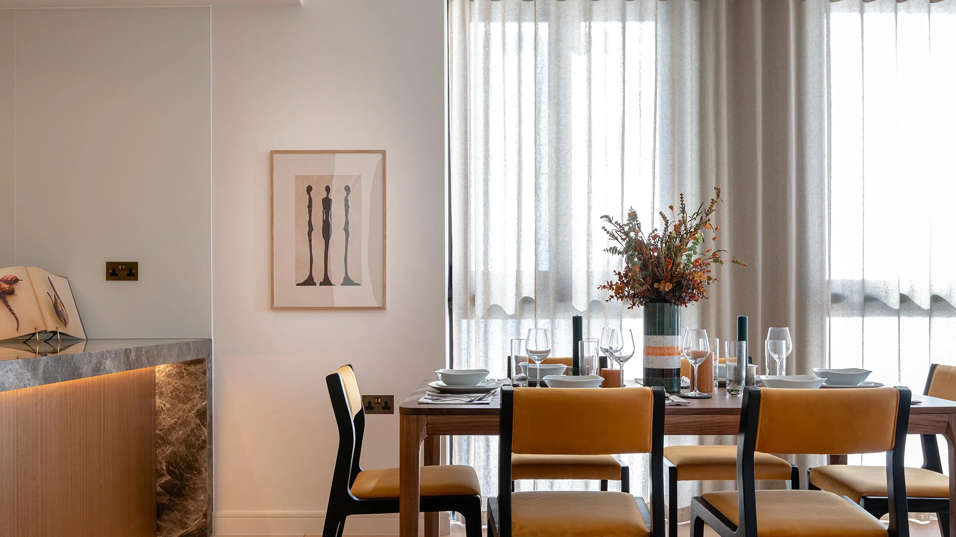 An elegant dining area styled by InStyle Direct featuring a wooden table set for four, mustard yellow chairs, and floor-to-ceiling sheer curtains that fill the room with natural light in Canary Wharf.