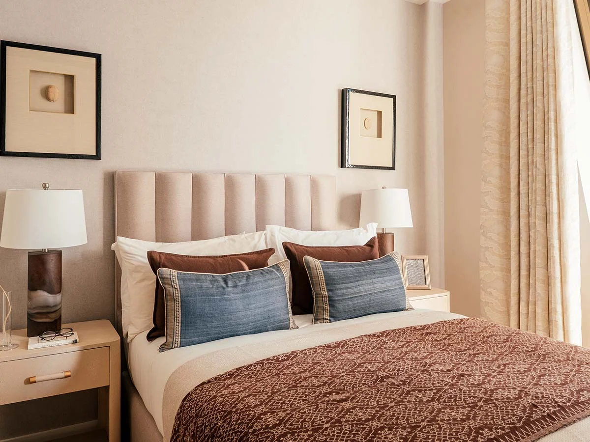  An elegant bedroom interior styled by InStyle Direct featuring a beige ribbed headboard, brown and denim-blue pillows, a patterned rust-colored throw, and symmetrical bedside lamps in Westminster.