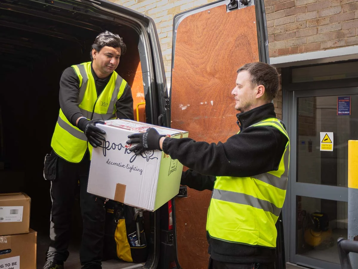 Professional delivery team members from InStyle Direct wearing high-visibility vests while carefully unloading a box of Pooky decorative lighting from a company van in London.