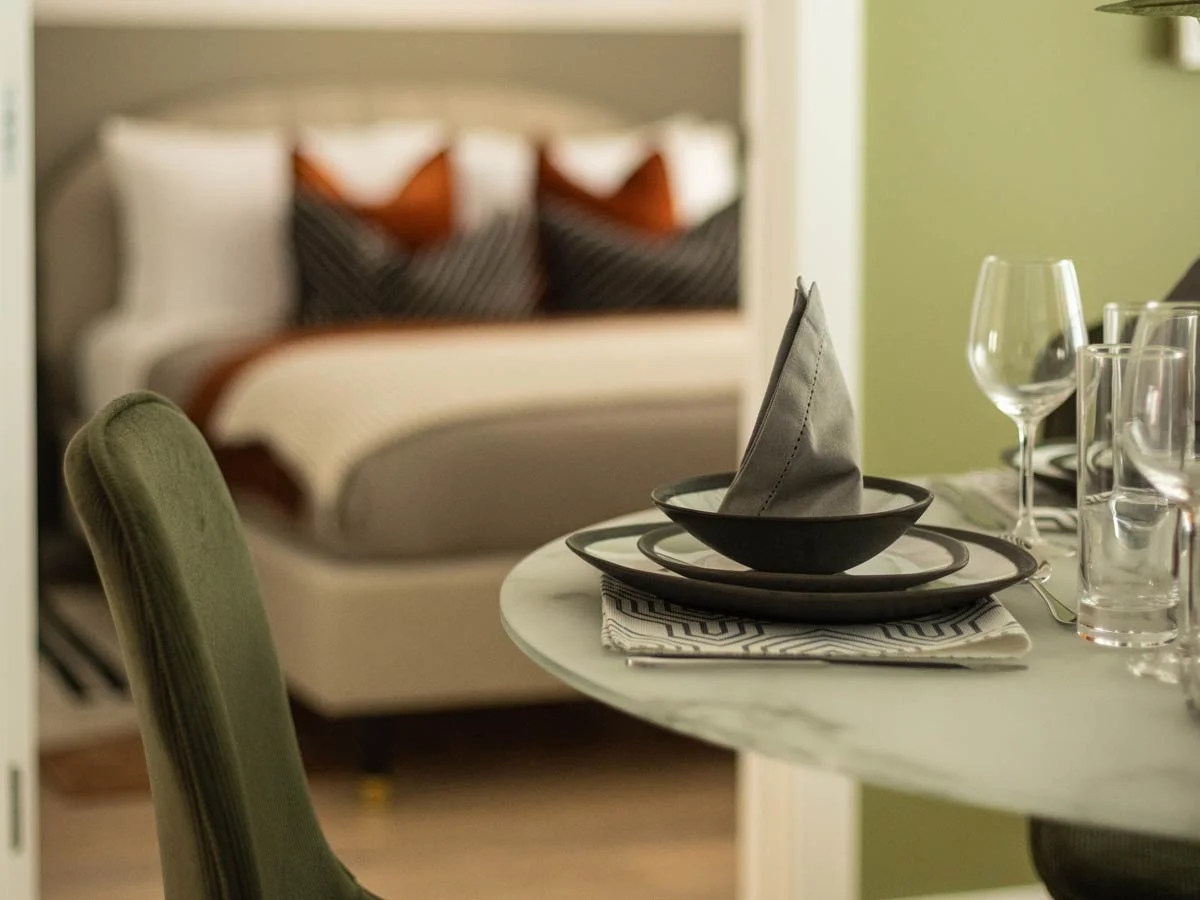 An artfully composed view from the dining area into the bedroom at the Verdica show flats, focusing on a beautifully set table in the foreground