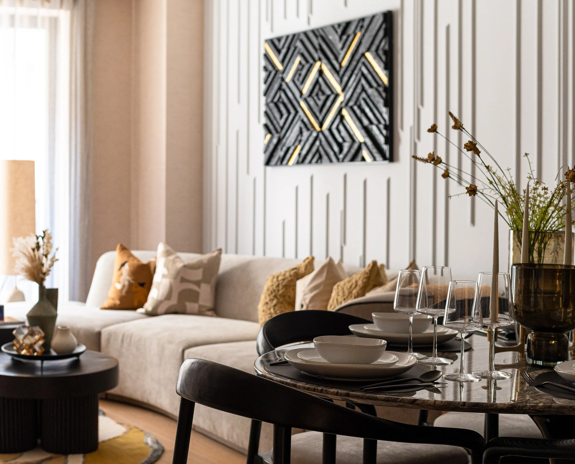 A luxury apartment interior styled by InStyle Direct featuring a round marble dining table with modern black chairs, a textured cream sofa, and 3D geometric wall art in Covent Garden.