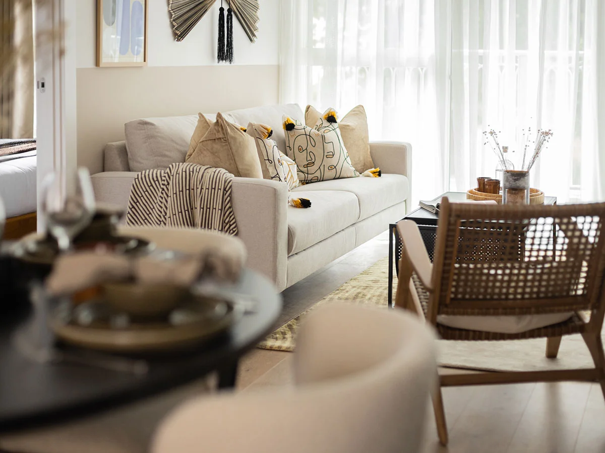 A luxury apartment living area styled by InStyle Direct featuring a cream-colored three-seater sofa with decorative cushions, a mid-century modern woven armchair, floor-to-ceiling sheer curtains, and a black coffee table in Marylebone