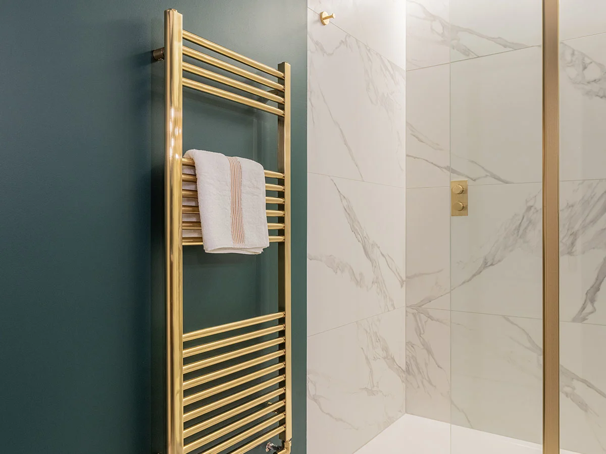 Luxury bathroom featuring brass heated towel rail and marble shower area in contemporary design