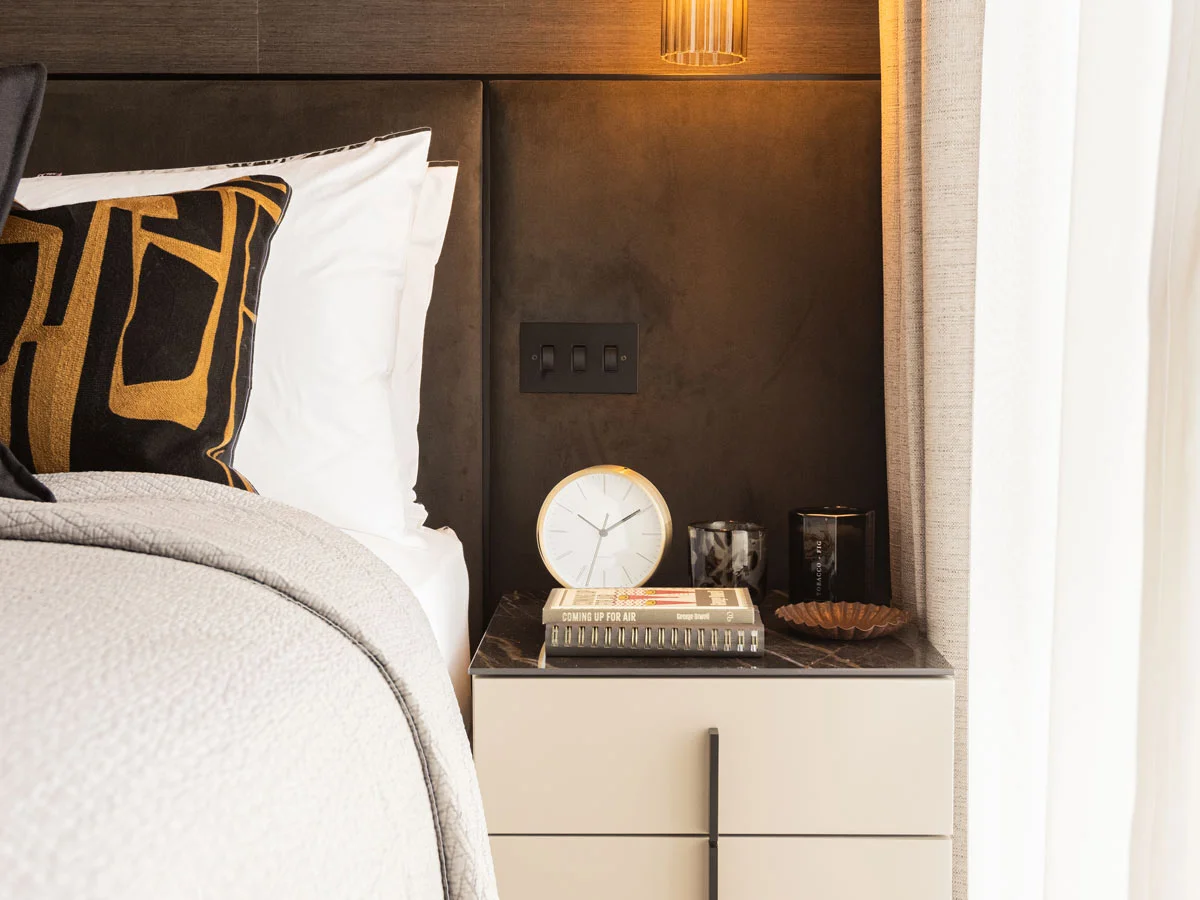 Modern bedside table with clock, books, and decorative items next to upholstered bed