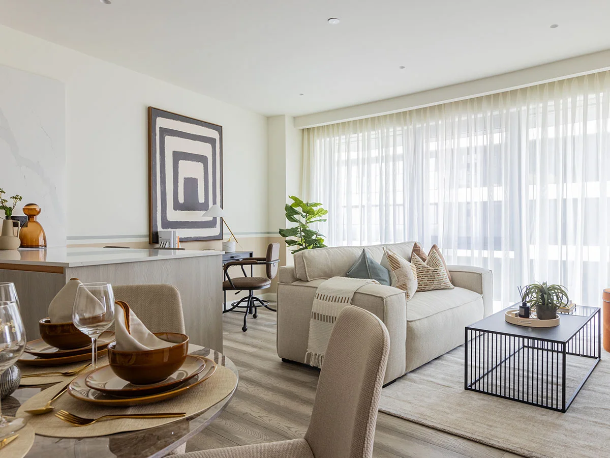 A sophisticated living area in Battersea featuring a deep blue velvet sofa, a slatted dark wood sideboard with a large circular gold mirror, and twin marble-top coffee tables styled by InStyle Direct