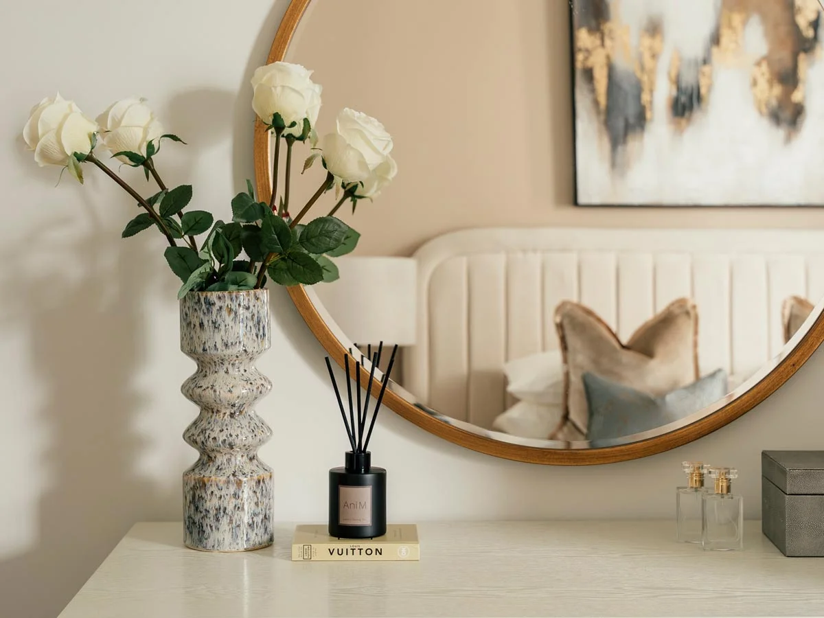 Bedroom vanity with decorative vase, white roses, diffuser, and round mirror