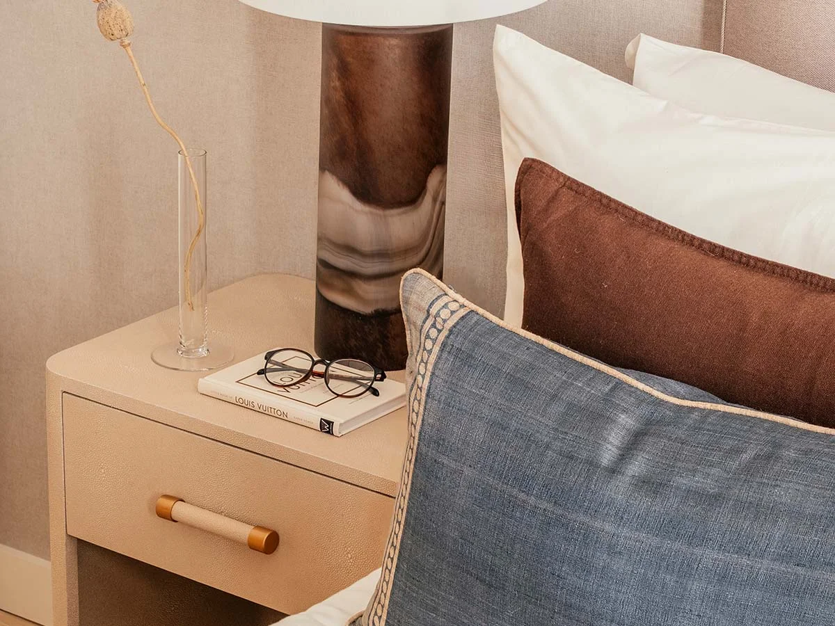 Luxury bedroom nightstand styling by InStyle Direct featuring a designer marble-effect table lamp, a Louis Vuitton coffee table book, and denim-blue pillows against a textured wallpaper backdrop in London