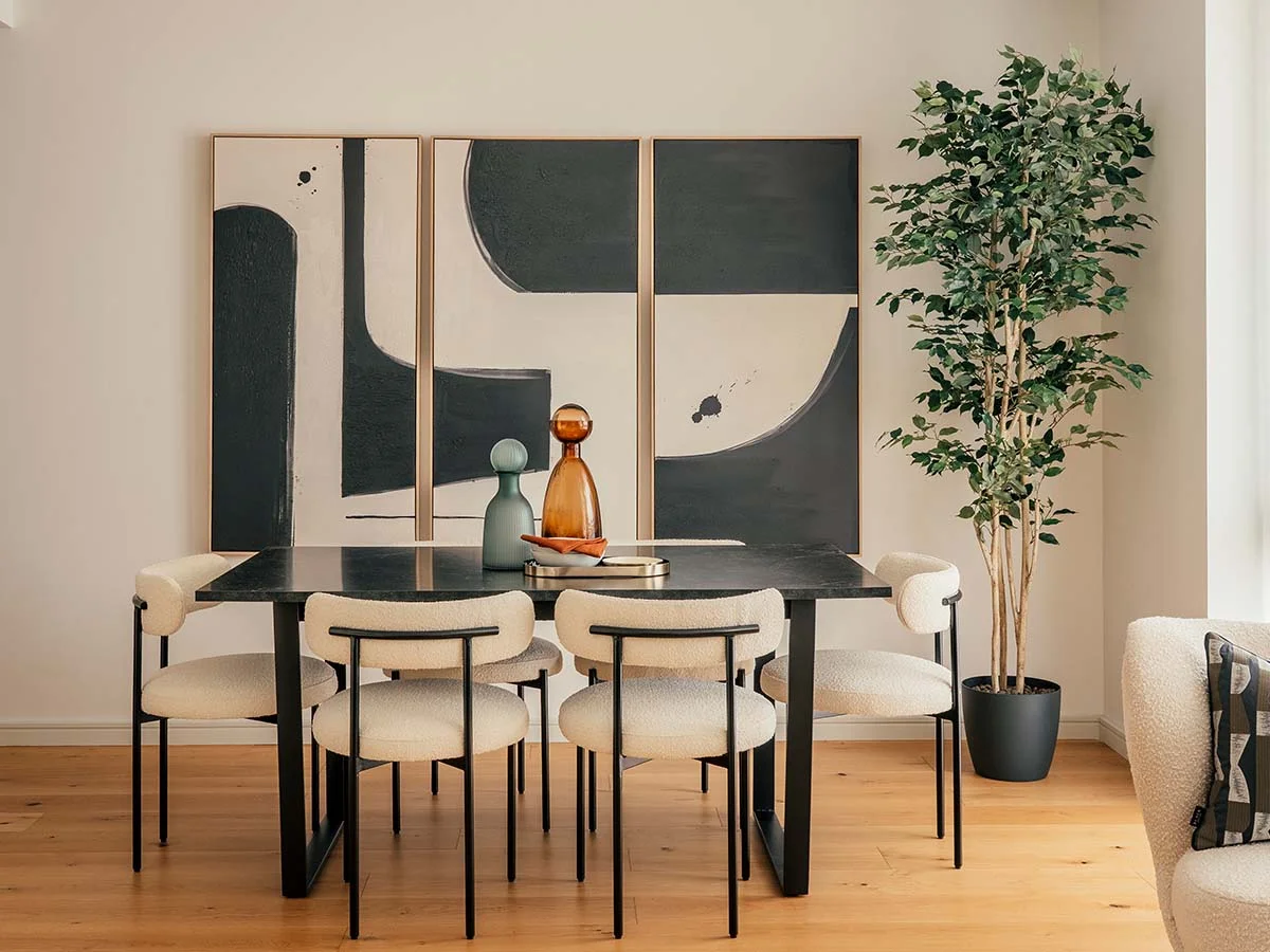 Modern dining table with four upholstered chairs, abstract wall art, and potted tree.