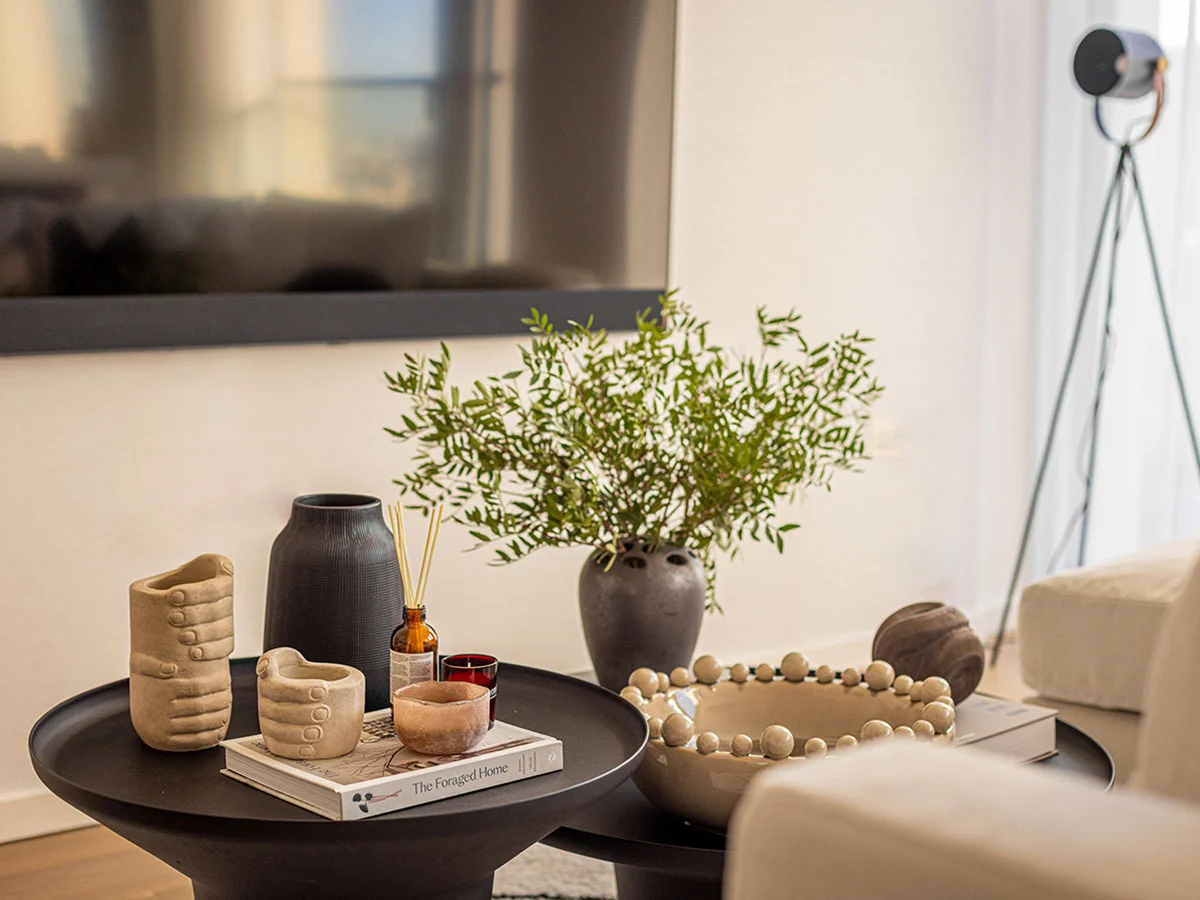 Close-up of luxury coffee table styling by InStyle Direct featuring unique hand-shaped ceramic planters, a black matte vase with greenery, and a beaded decorative bowl on a matte black tiered table in Southbank.