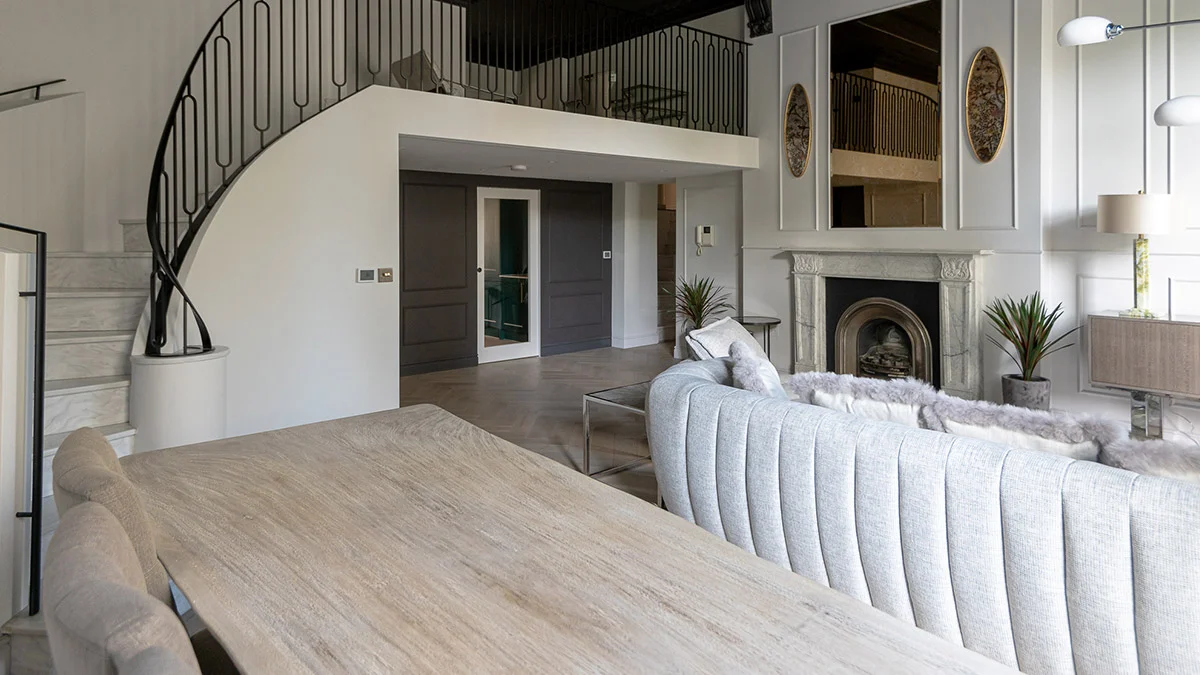 A luxury mezzanine-style living area styled by InStyle Direct featuring a large light grey textured sofa, a classic marble fireplace with a large mirror above, and a light-toned wooden dining table in Notting Hill.