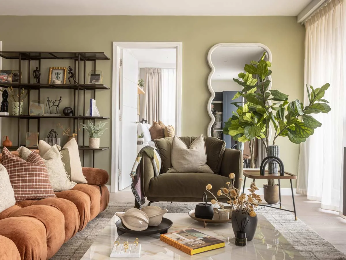 A luxury living room styled with a homeowner furniture package by InStyle Direct, featuring an olive green armchair, a rust-colored modular sofa, a large wavy floor mirror, and a bespoke black metal shelving unit.