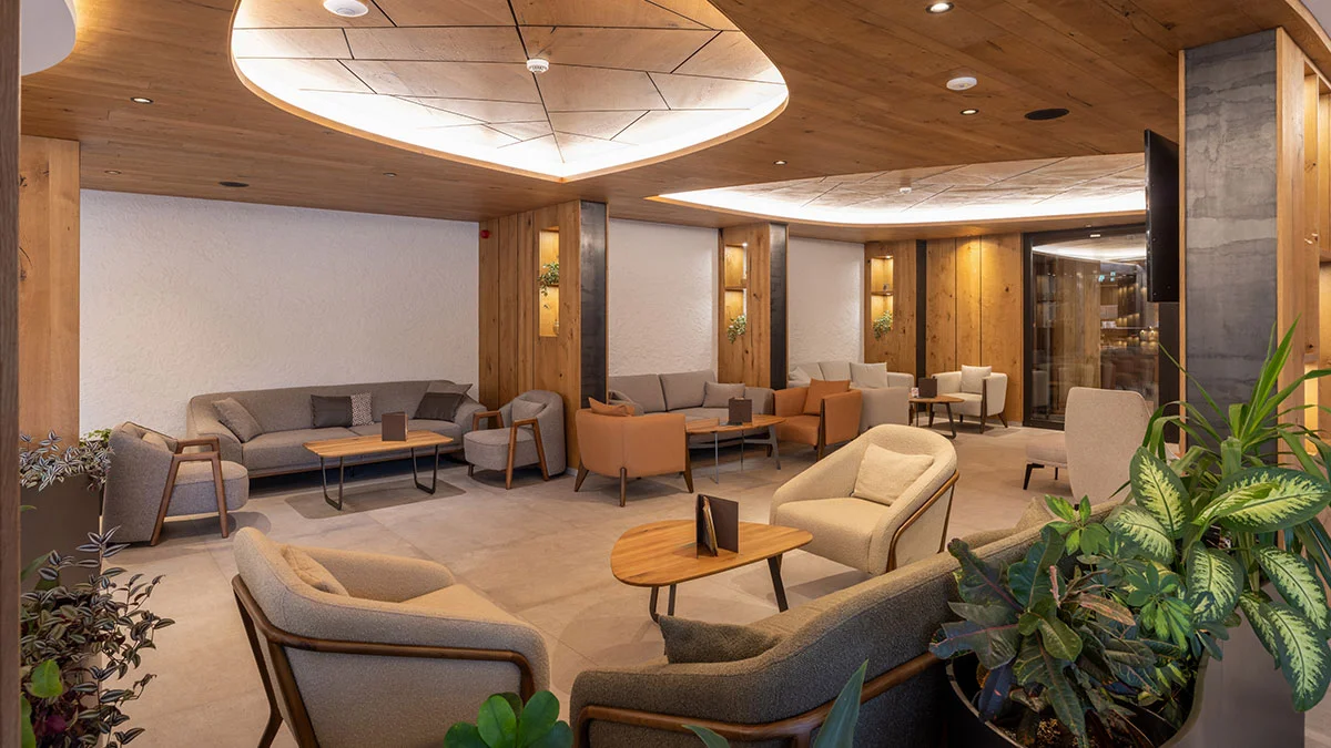 A luxury hotel lounge area styled by InStyle Direct featuring oak-panelled walls and ceilings, recessed heart-shaped lighting, and a mix of neutral and terracotta upholstered armchairs and sofas.