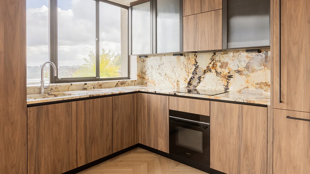 A luxury kitchen renovation in St. John"s Wood by InStyle Direct showcasing warm wood cabinetry, a dramatic gold-veined marble splashback and countertop, and modern integrated appliances with chevron wood flooring.