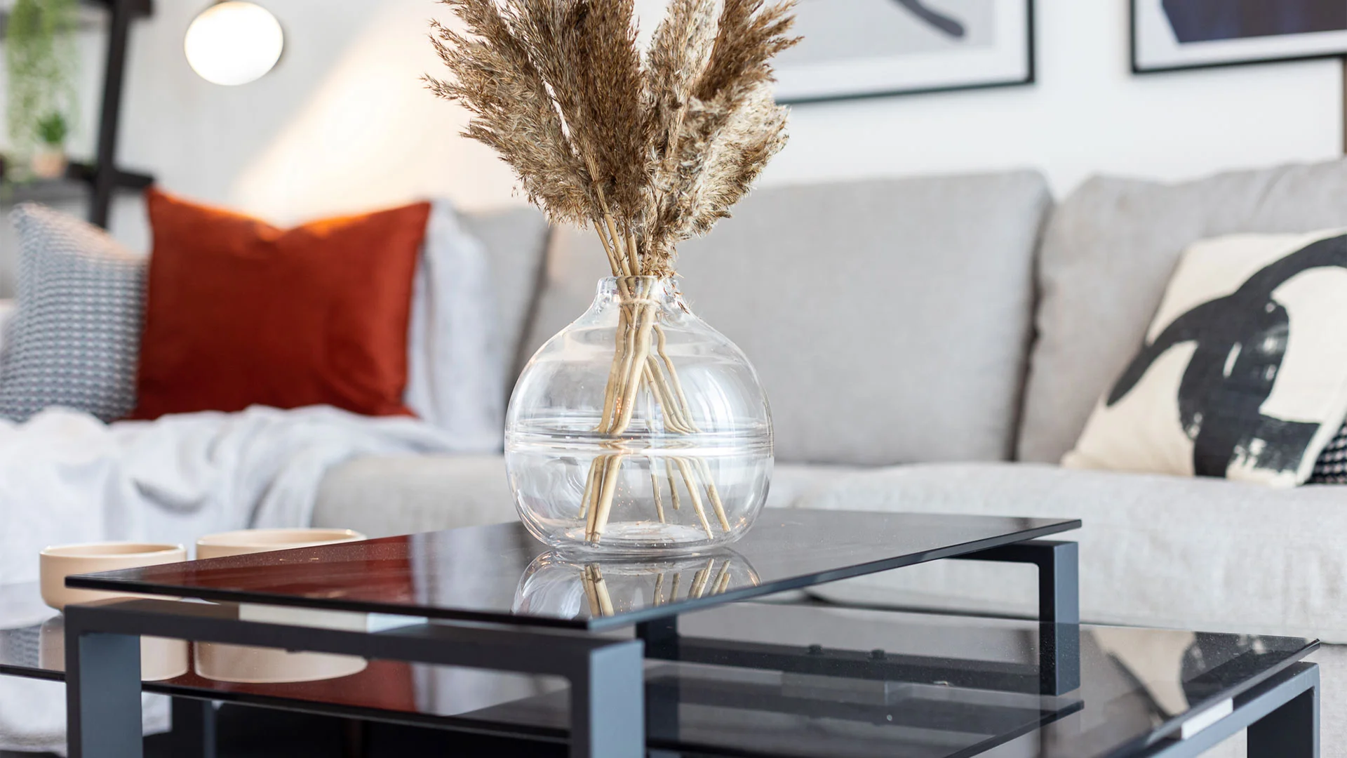 Luxury living room styling by InStyle Direct featuring a black glass-top coffee table with a round glass vase containing dried pampas grass, set against a light grey sofa in Silvertown.