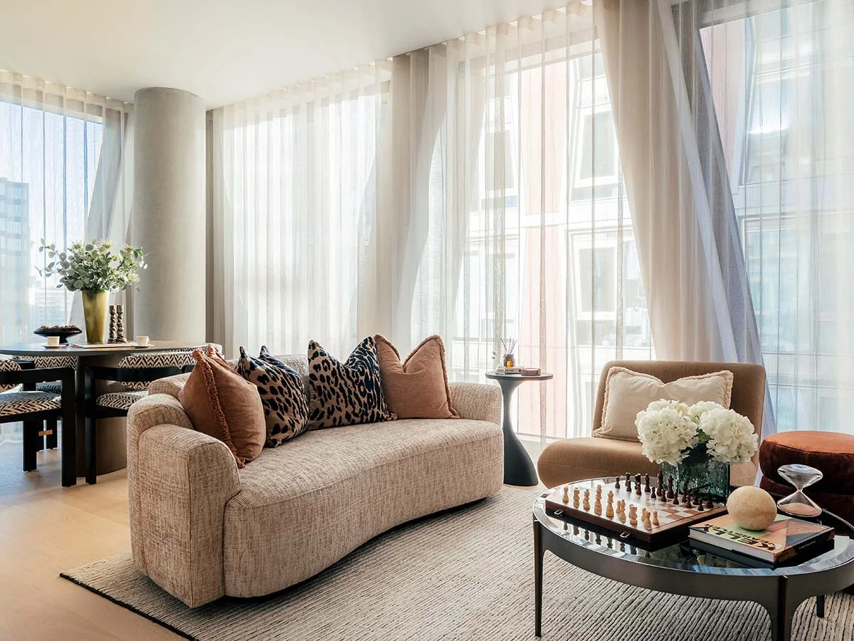 A luxury open-plan living room styled by InStyle Direct featuring a curved beige sofa with leopard print cushions, a marble coffee table with a chessboard, and floor-to-ceiling sheer curtains in Westminster.