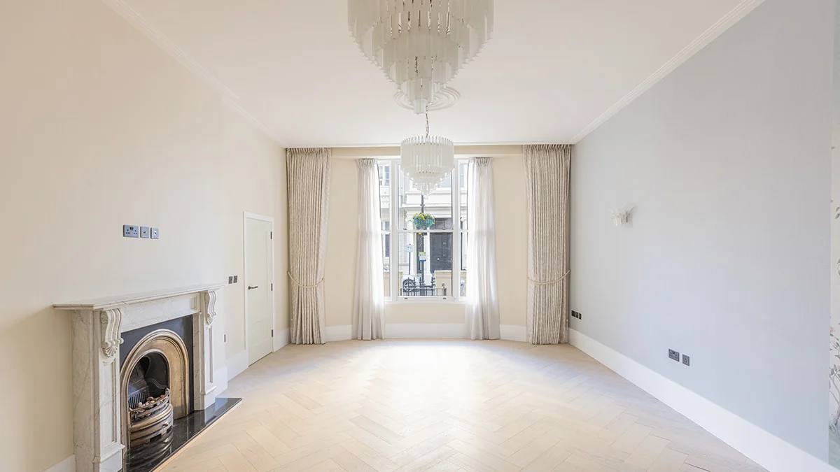 A stunning living room renovation by InStyle Direct featuring a restored period marble fireplace, light herringbone wood floors, bespoke neutral curtains, and a grand multi-tier glass chandelier in Bayswater.