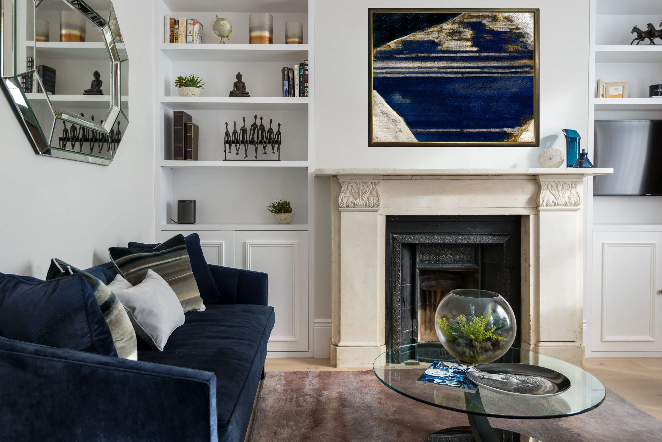 A luxury living room styled by InStyle Direct featuring a deep blue velvet sofa, a classic white marble fireplace with a mirror above, and built-in shelving with curated ornaments in West Hampstead.