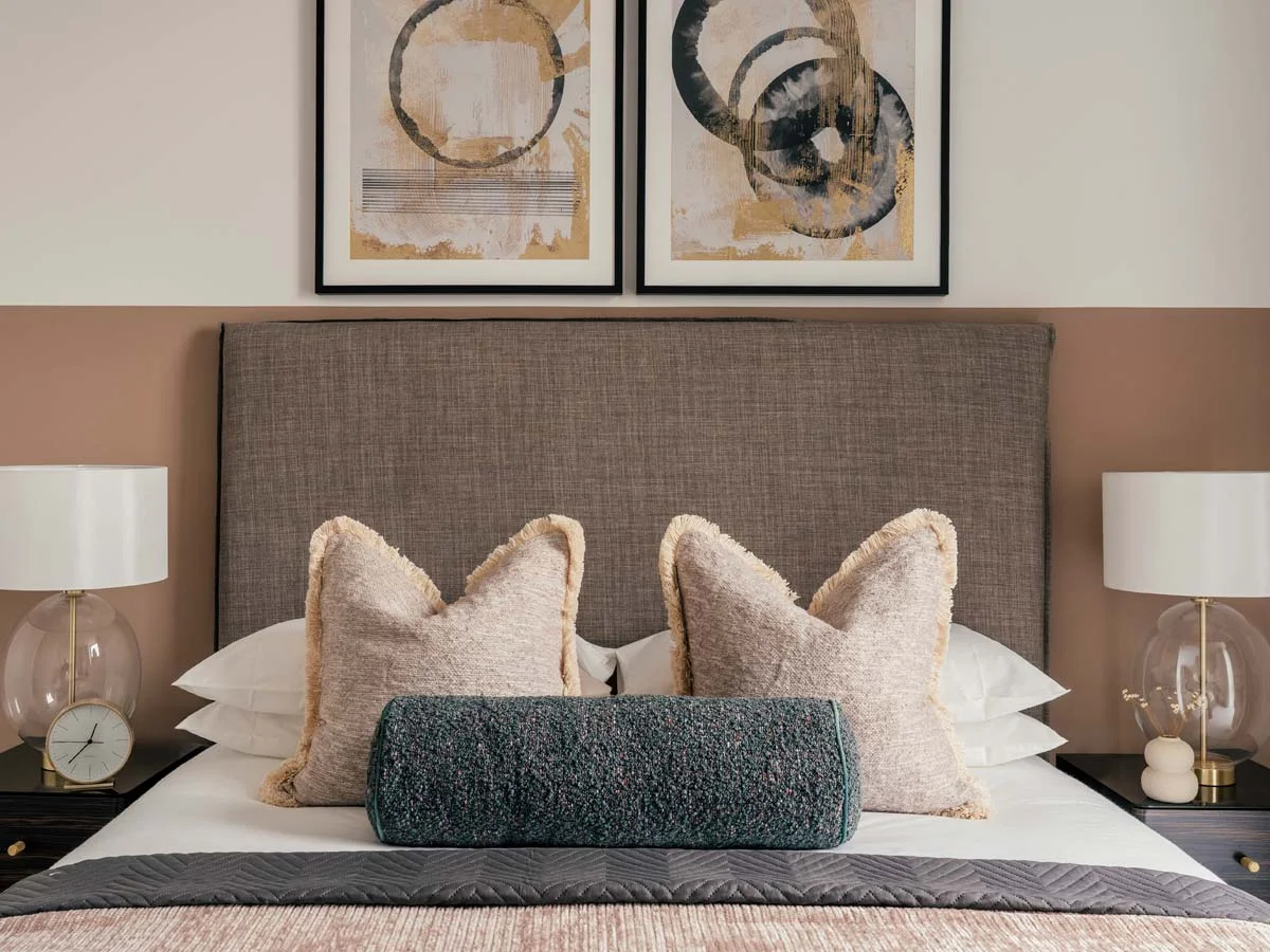 A luxury master bedroom styled by InStyle Direct featuring a tall textured grey headboard against a terracotta feature wall, accented by a teal bolster cushion, fringed pillows, and elegant glass globe bedside lamps
