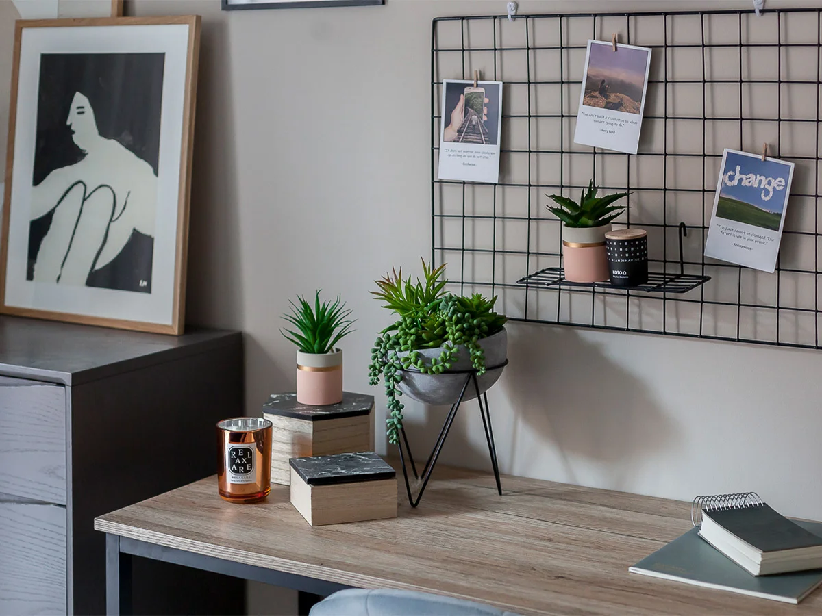 A minimalist home office desk styled by InStyle Direct featuring a black wire wall grid for photos, small potted succulents in pink and grey ceramic, and a modern wooden workspace in London.