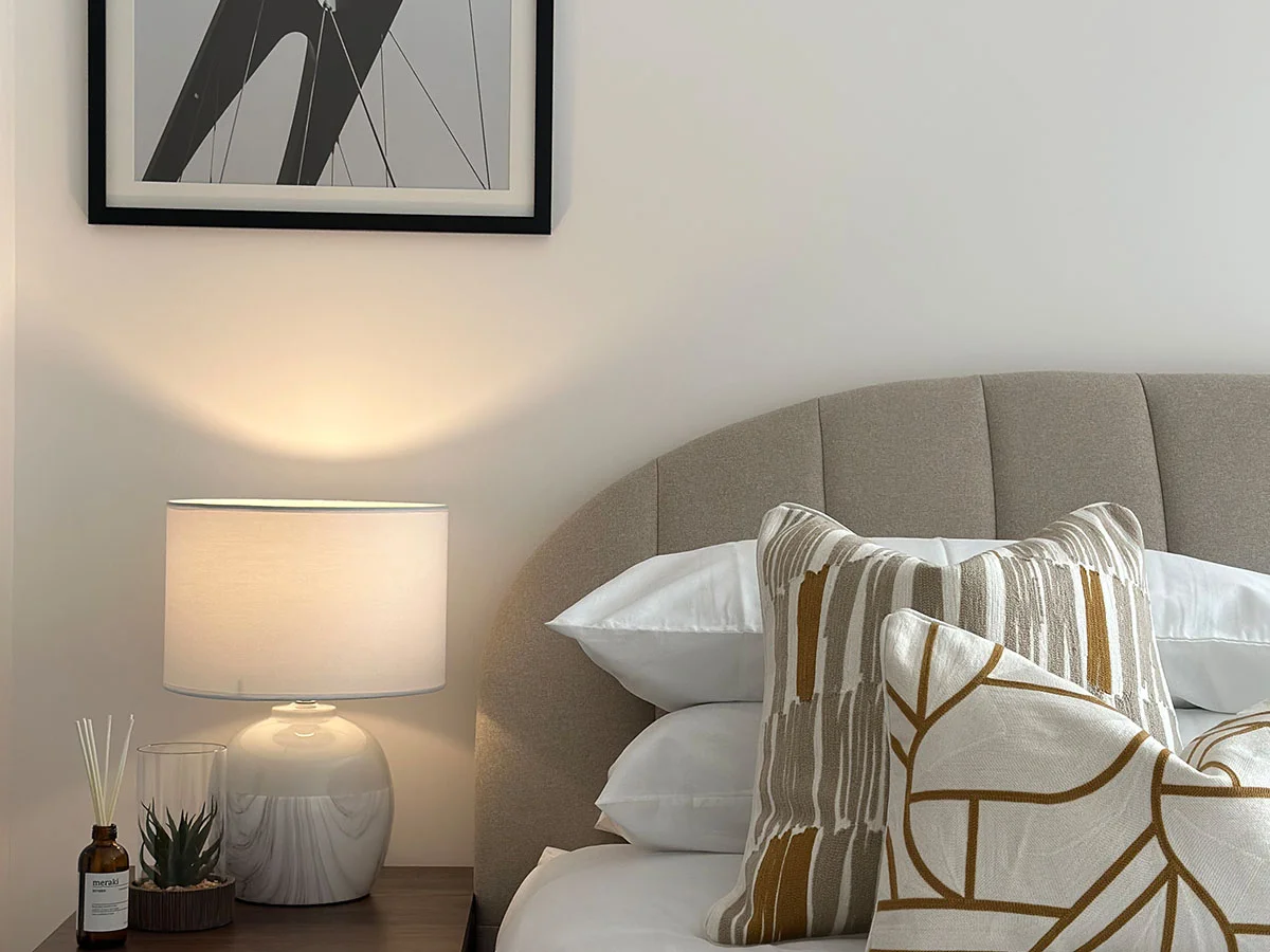 Partial view of modern bedroom with half bed, styled cushion pillows, and bedside table lamp