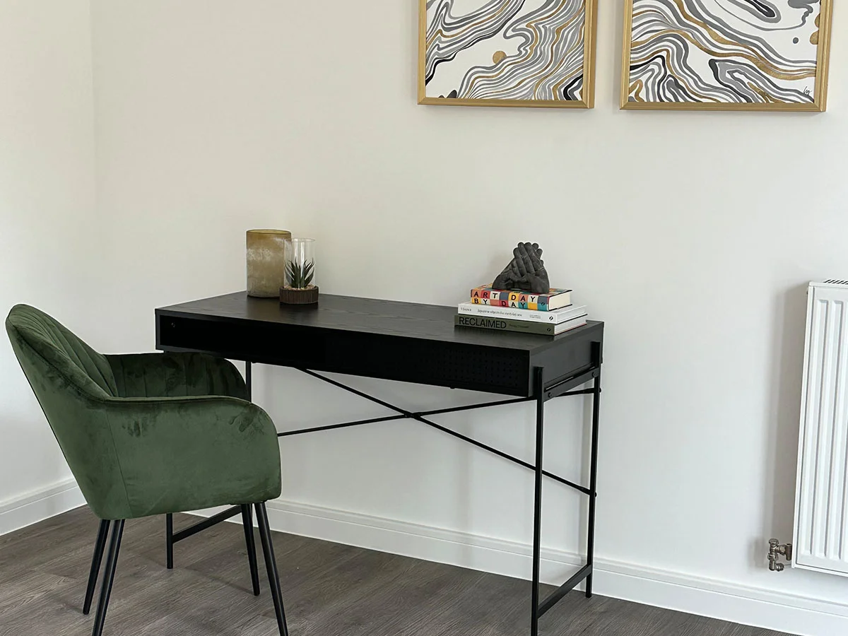 Modern home office setup with black desk, green velvet chair, decorative books, and minimalist wall art