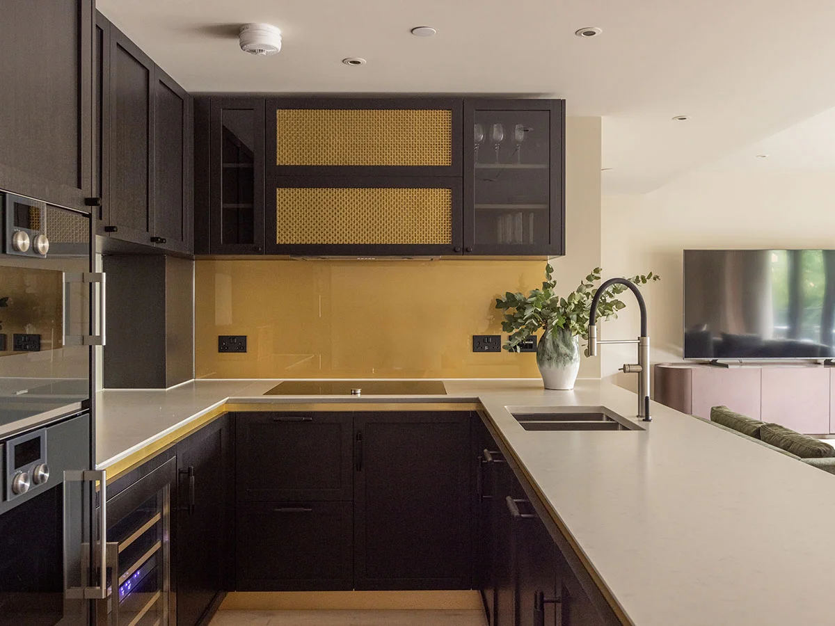 Sleek dark kitchen cabinetry with gold accents and a mustard yellow backsplash