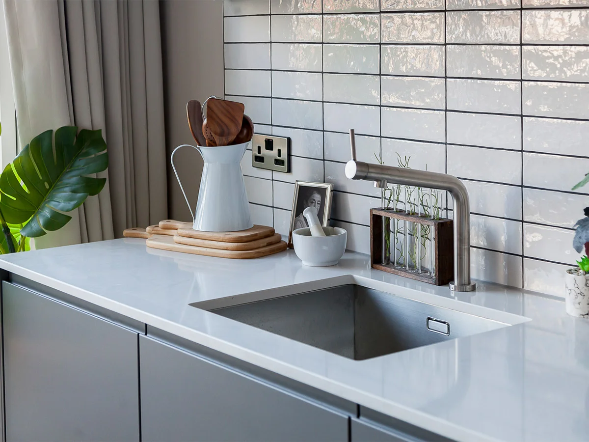 A modern kitchen styled by InStyle Direct featuring a white marble worktop, a stainless steel undermount sink with a contemporary faucet, and glossy white subway wall tiles in Stratford.