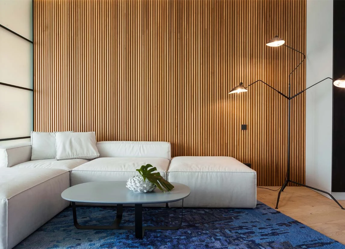 A modern living room styled by InStyle Direct featuring a floor-to-ceiling vertical wood slat feature wall, a low-profile white sectional sofa, a textured blue rug, and a multi-arm industrial floor lamp in Islington.