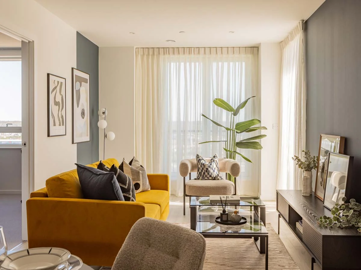 A wide view of the modern living room at Meridian One, featuring a vibrant yellow velvet sofa, dark grey accent walls, and a large indoor plant