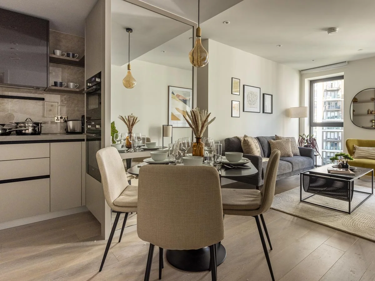A bright, open-plan apartment at Westmont, London, showing the dining area and a mirrored wall that reflects the modern living room and kitchen
