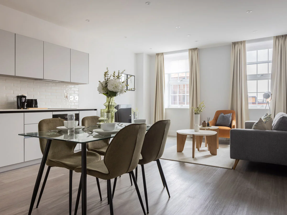Modern open-plan kitchen and living room with glass dining table and grey sofa